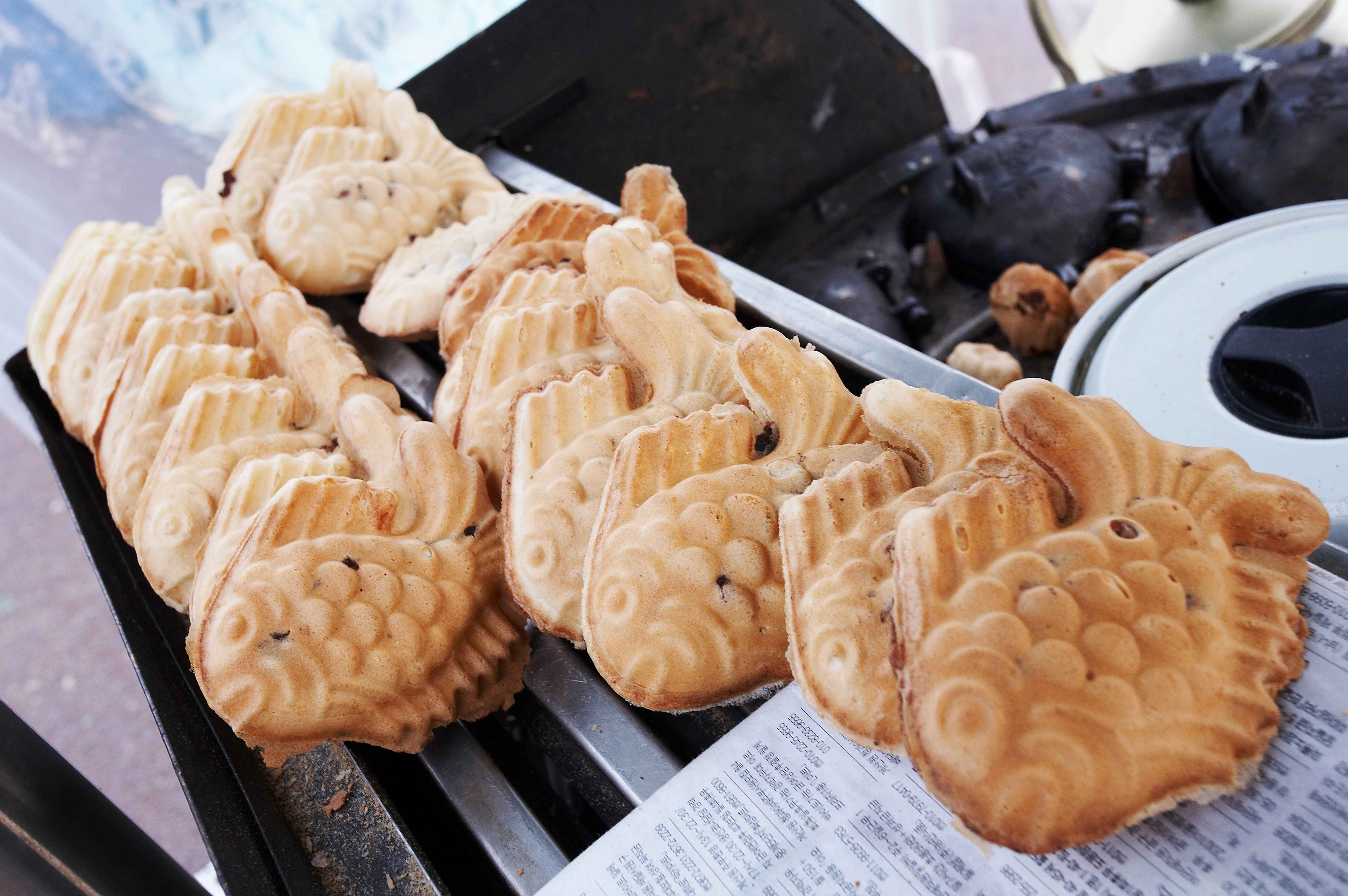 Freshly baked fish-shaped pastries arranged on a tray near a mold and newspaper.