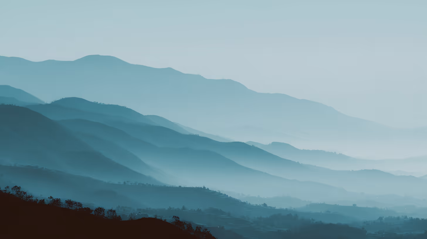 Paysage de montagnes en couches bleutées avec une légère brume sous un ciel clair.