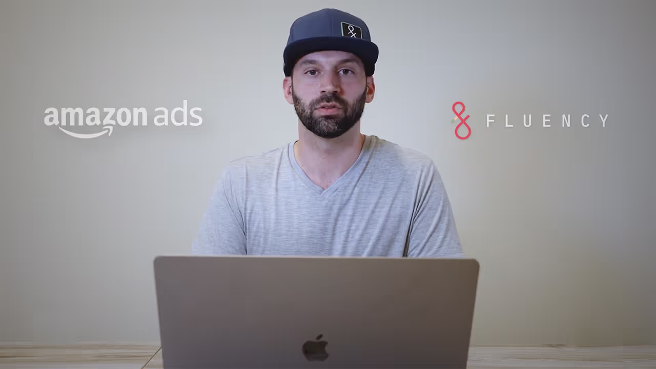 Man wearing a blue cap and gray shirt sitting behind a laptop with Amazon Ads and Fluency logos on the wall behind him.