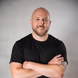 Smiling bald man with a beard wearing a black t-shirt and crossing his arms.