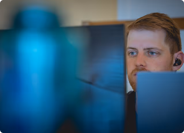 Focused man with earbuds looking at a computer screen in an office setting.