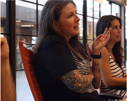 Woman with long dark hair and tattooed forearm speaking during a meeting in a modern office.