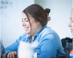 Smiling woman in a blue shirt concentrating on a laptop during a meeting.