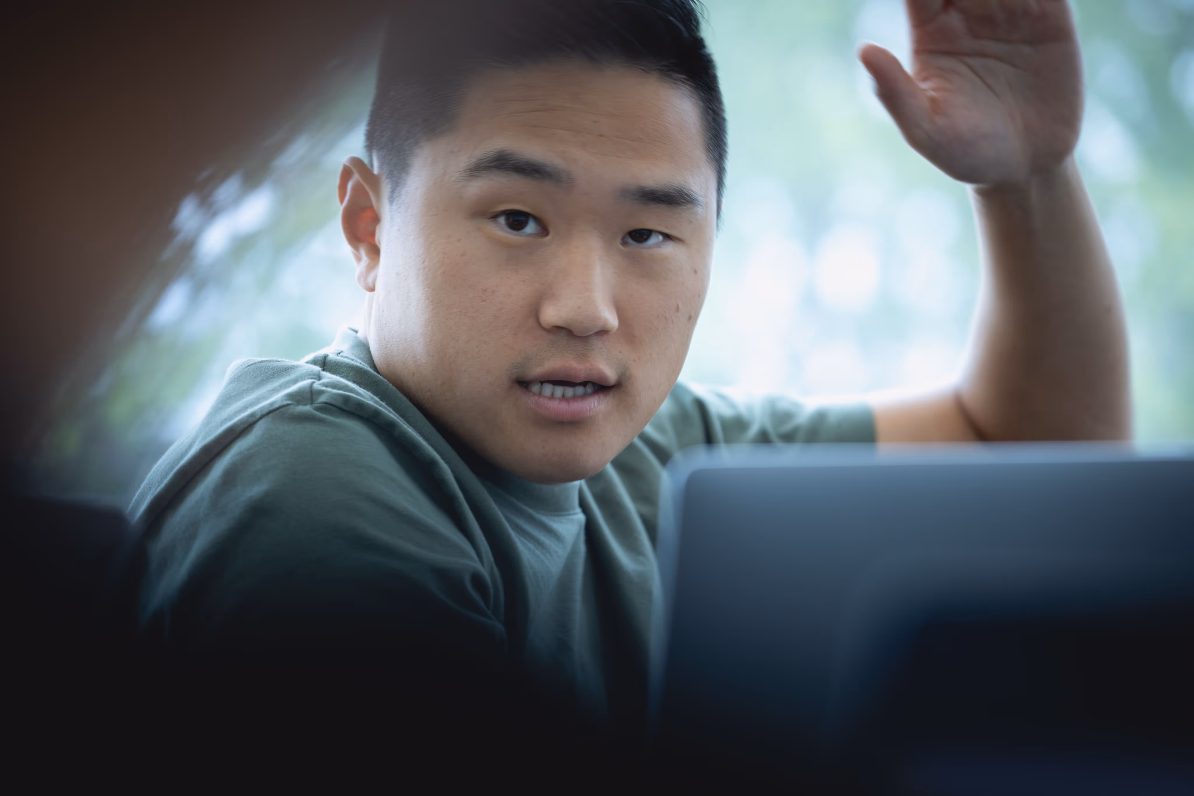 Man raising his hand while speaking during a discussion with a laptop visible in the foreground.