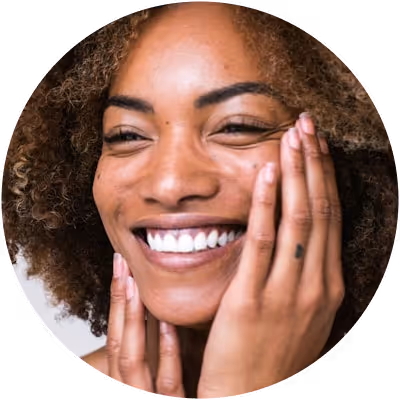 Close-up of a smiling woman with curly hair holding her face with both hands.
