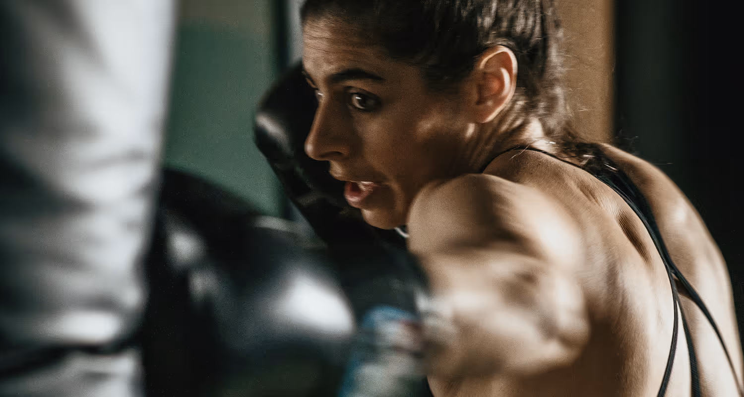 Woman with braided hair intensely throwing a punch while boxing.
