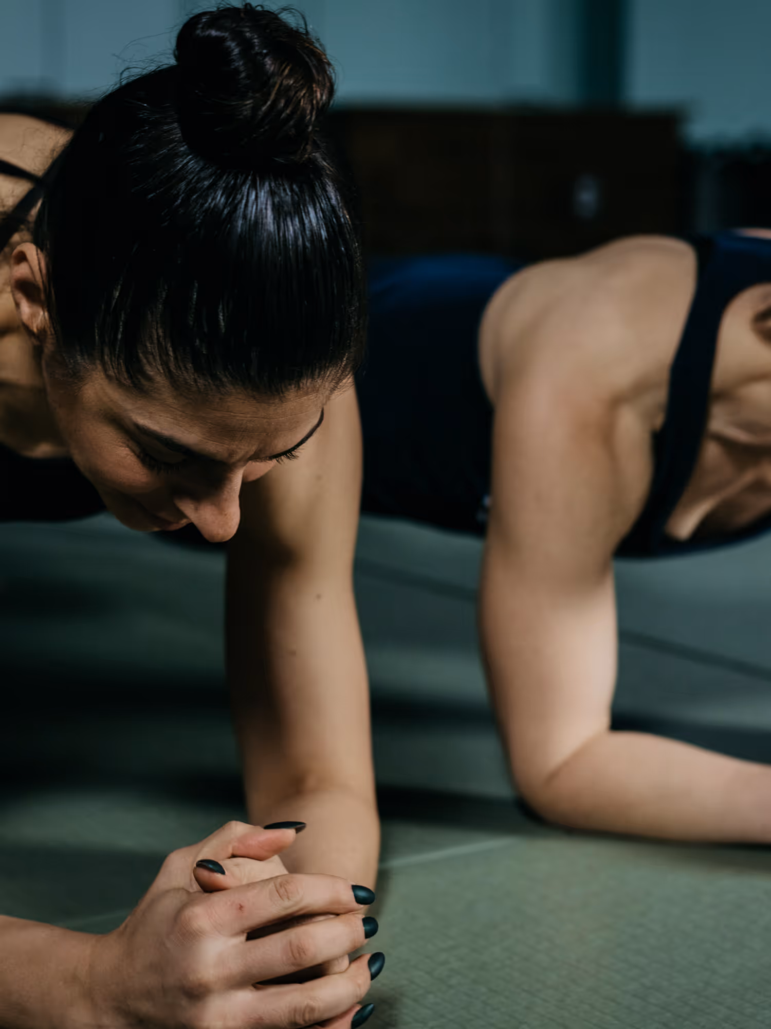 Two women in a plank position on a mat, focusing on their forearms and hands clasped together.