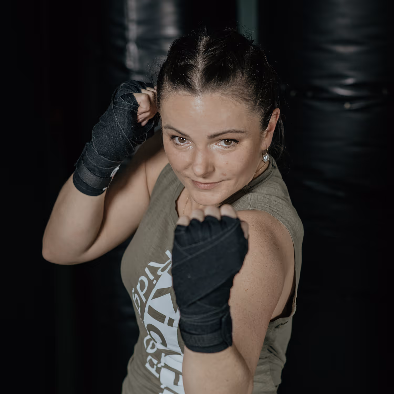 Woman with braided hair wearing fingerless hand wraps in a boxing stance looking confidently at the camera.
