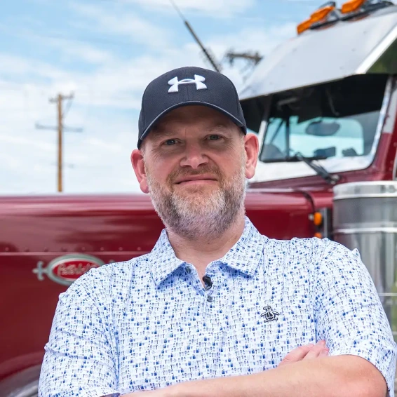 A man with a trucker hat smiling in front of his semi truck