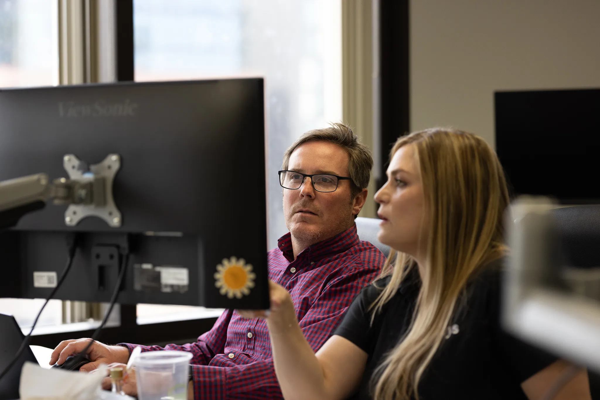 Office setting with two people collaborating at a computer, smartphone displaying user interface features, customer service, setup tutorial.