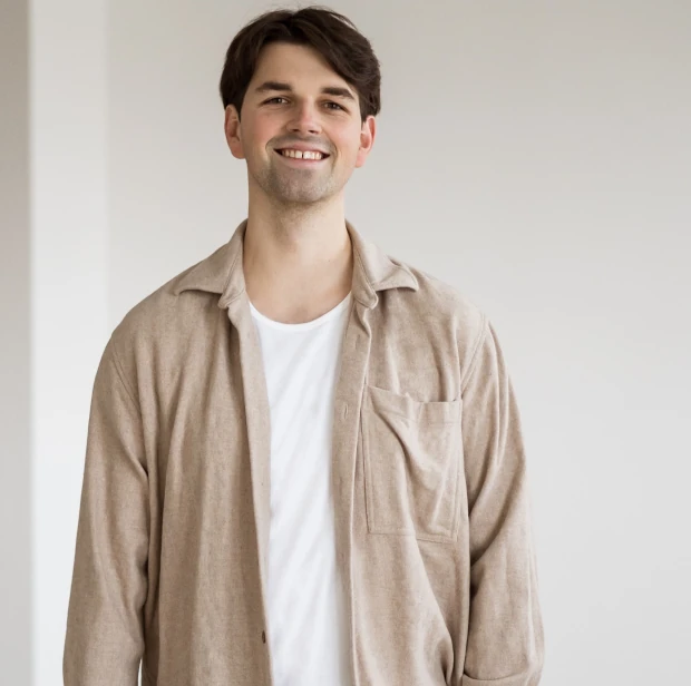 Anwalt Domenic Trybull lächelt und trägt ein hellbraunes Hemd über weißem T-Shirt vor neutralem Hintergrund.