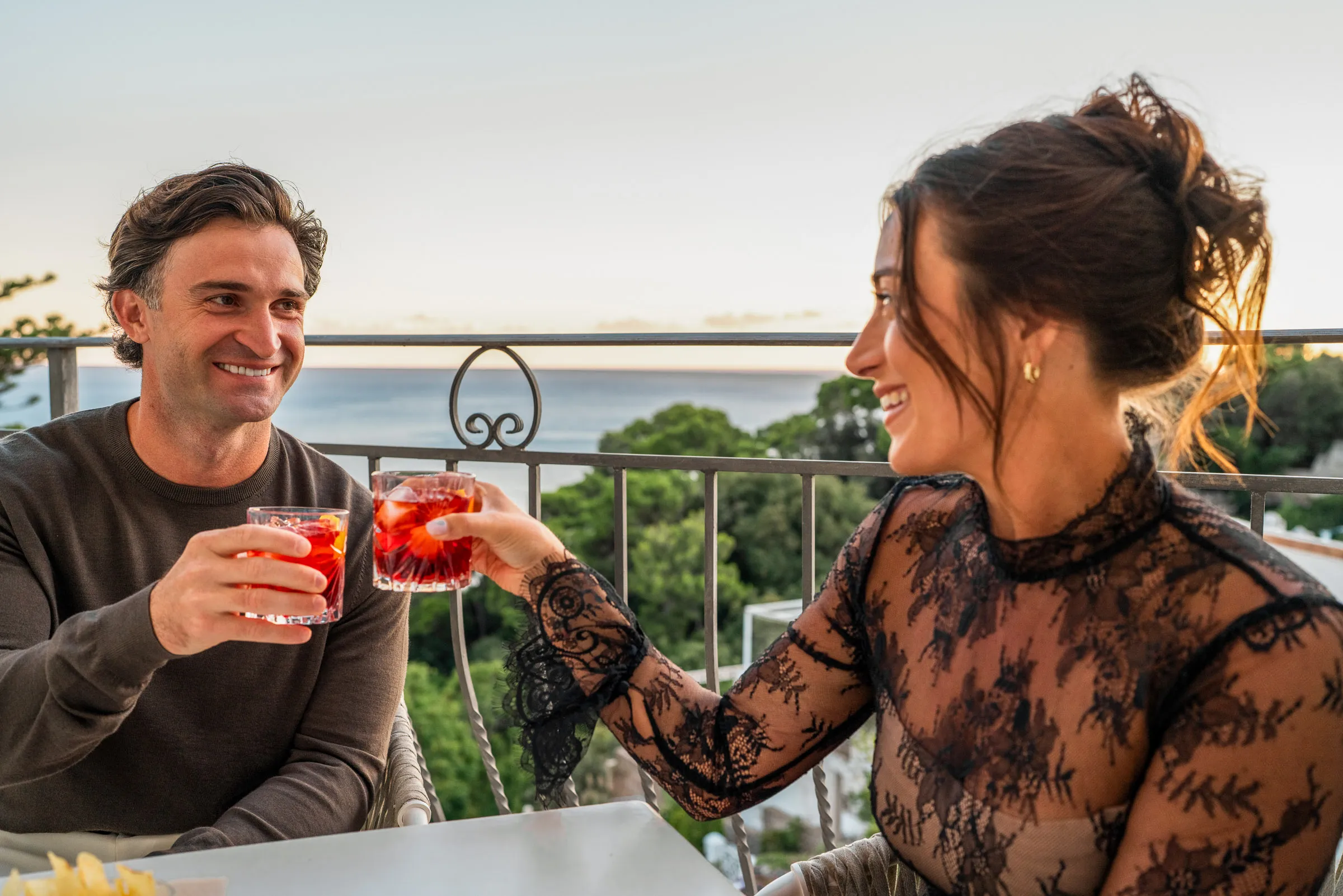 Couple enjoying sunset with cocktails on balcony overlooking ocean
