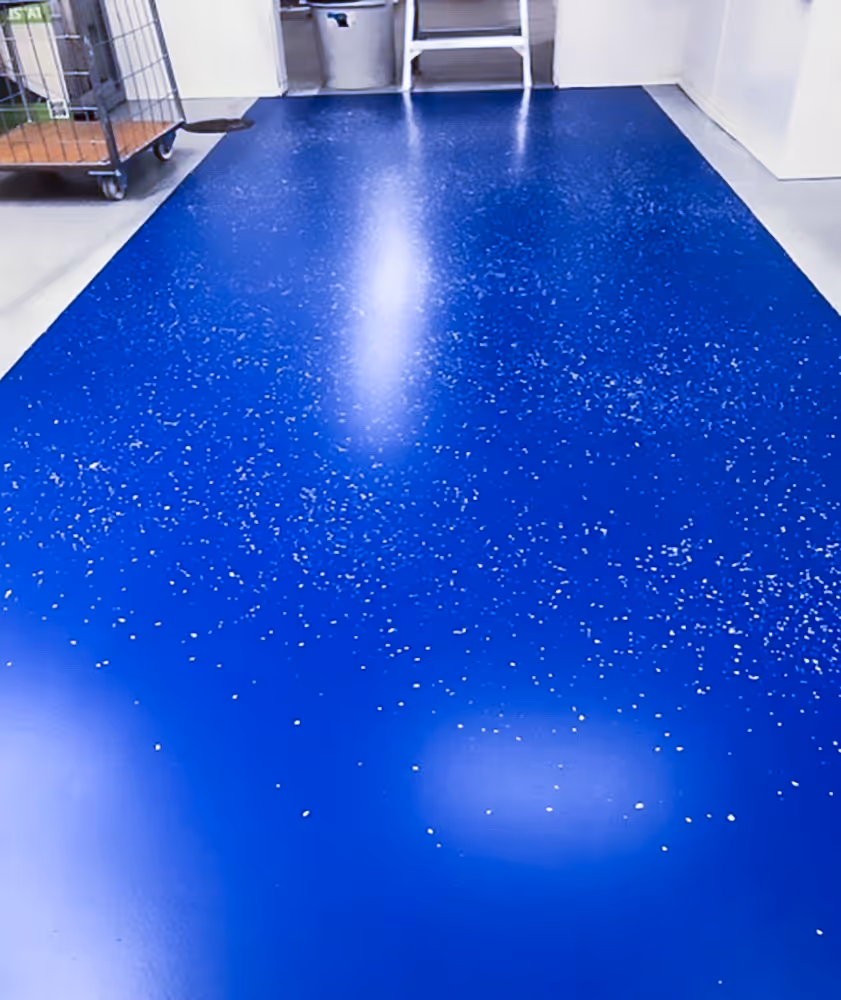Kiiltävä sininen muovimatto, jossa on valkoisia pilkkuja, teollisessa tilassa.