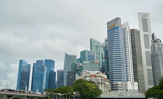 City skyline featuring modern skyscrapers including HSBC and Maybank buildings under a cloudy sky.
