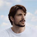 Young man with dark hair and beard wearing a white shirt looking to the side against a blue sky with clouds.