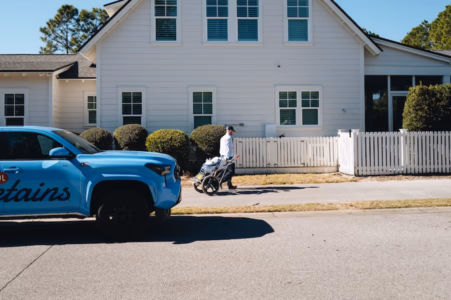 Man in white shirt pushing pool cleaning equipment on a cart beside a light blue pickup.