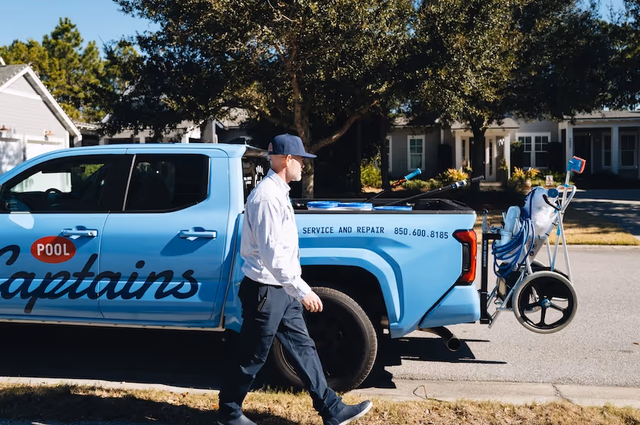 Man in uniform walking beside a light blue Pool Captains service truck equipped with pool cleaning tools and equipment.