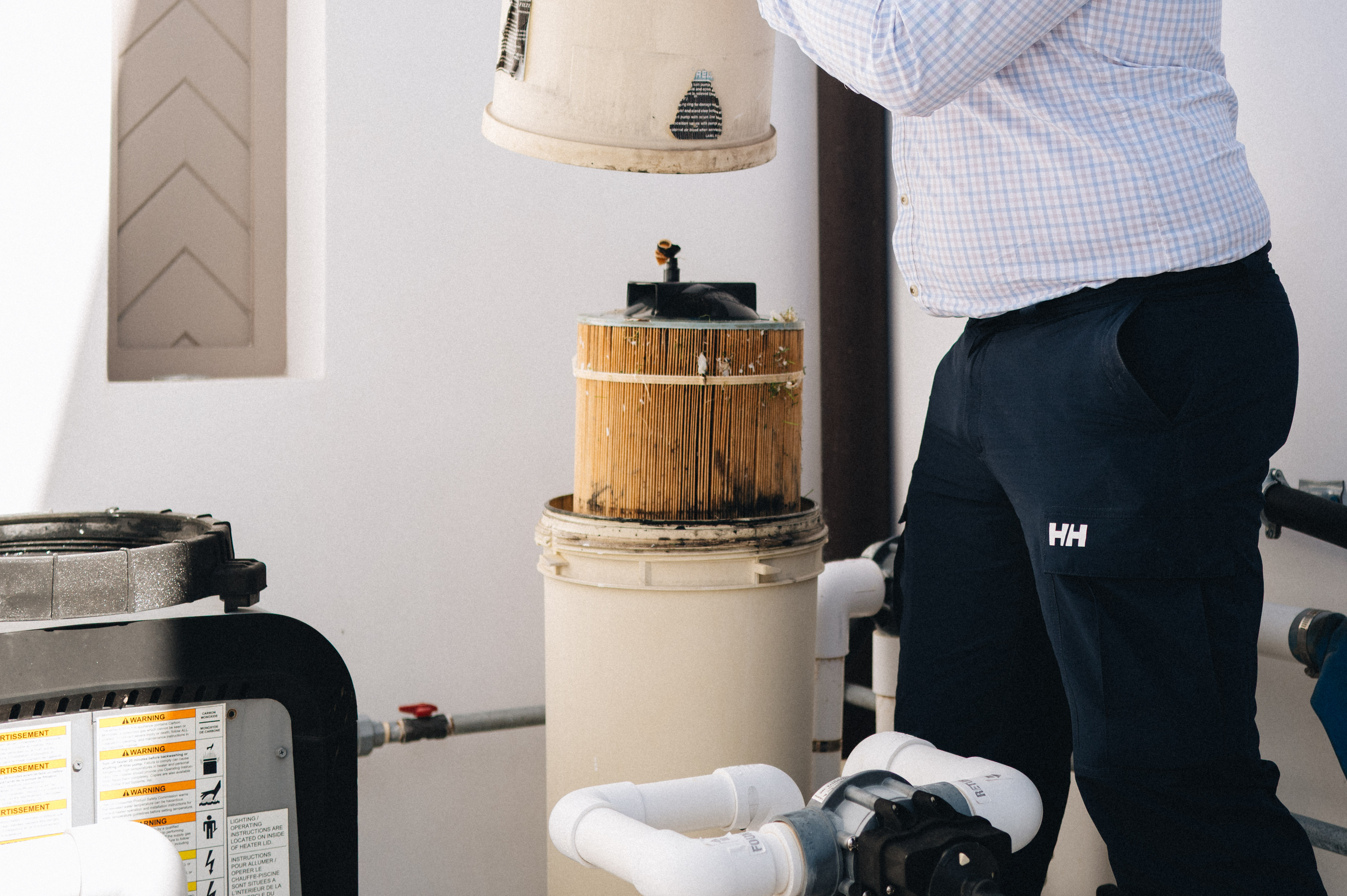 Pool Captains technician lifting the lid off an open cartridge filter beside a heater and pump on a residential equipment pad
