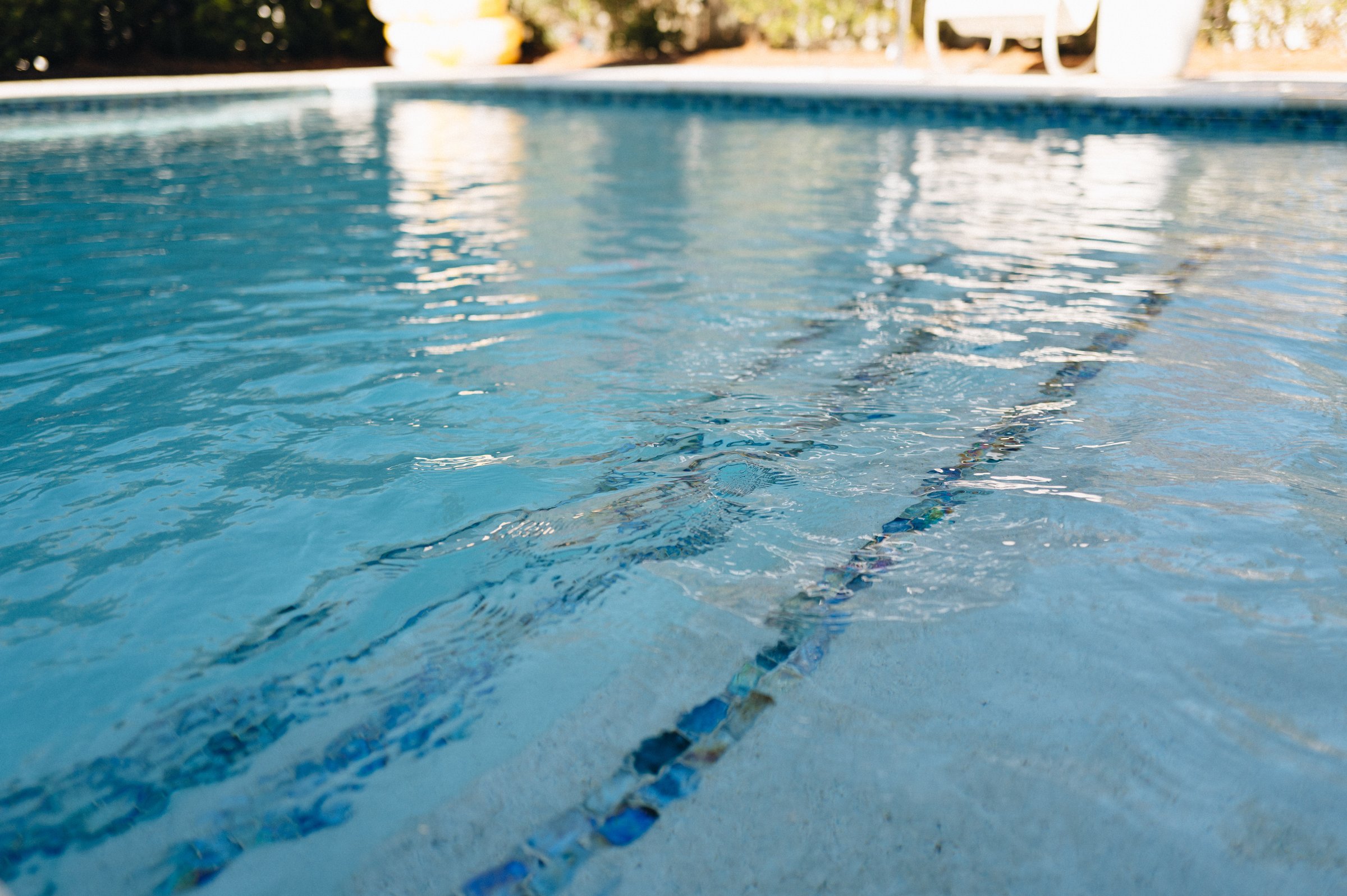 Clear light-blue Emerald Coast pool water looking across submerged steps with blue mosaic tile accents in bright sunlight