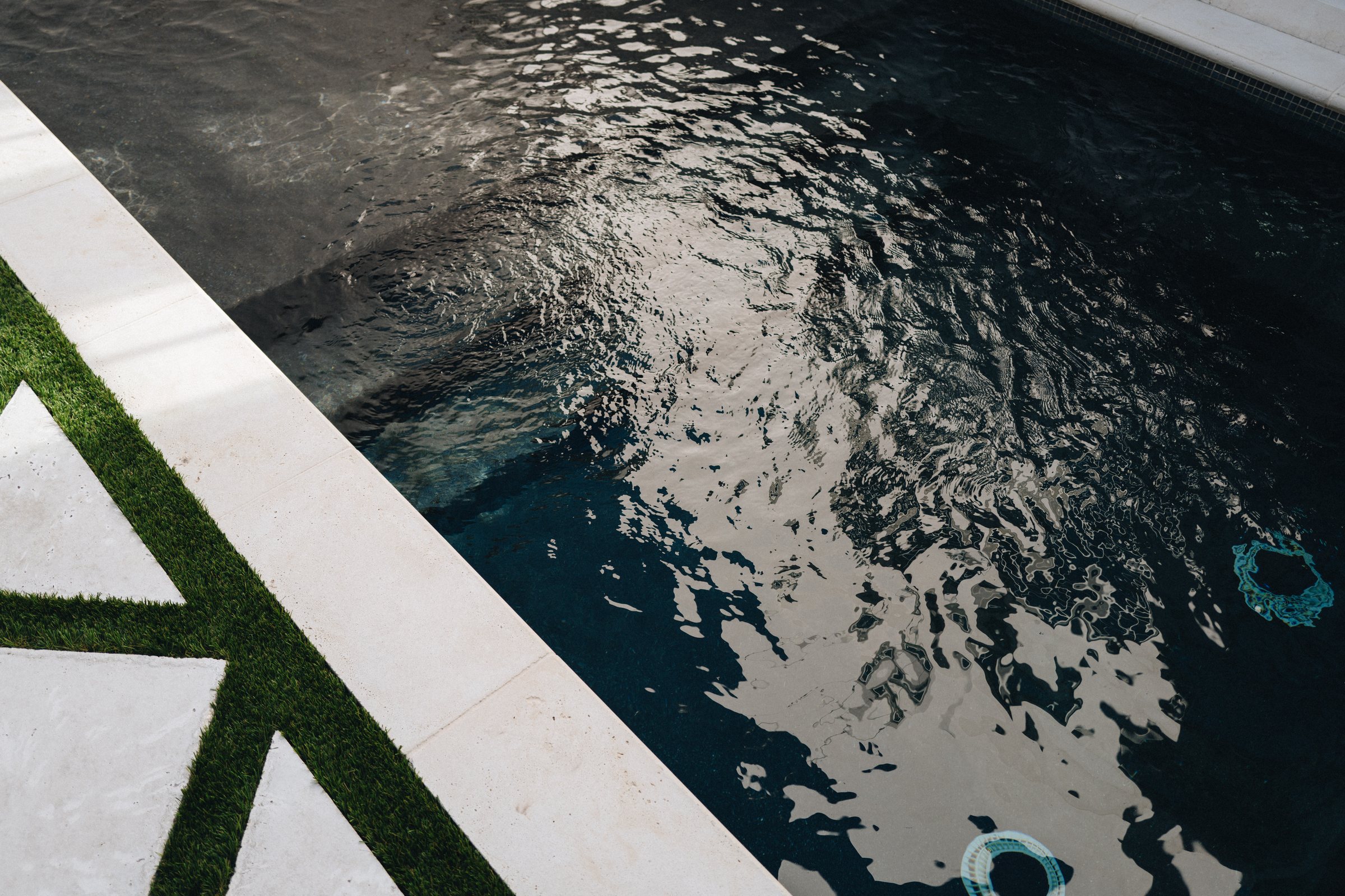 Clear dark-finish backyard pool with white travertine coping beside a turf-and-paver deck in Emerald Coast sun