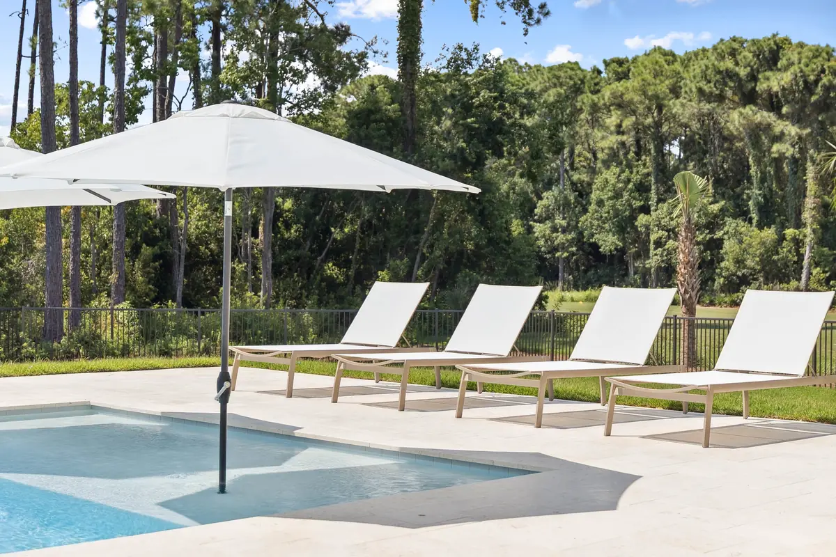 Clean, clear pool with white lounge chairs and a shade umbrella at a Destin home