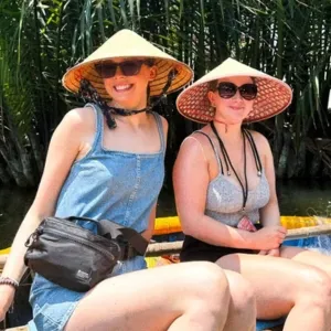 Two women wearing traditional conical hats and sunglasses sitting outdoors with greenery in the background.