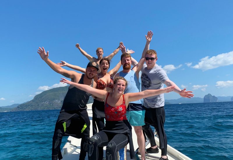 Camp participants pose with their arms out on a boat in the ocean