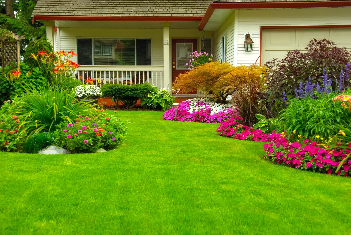 Front yard of a house with bright green lawn and colorful flower beds along the walkway.
