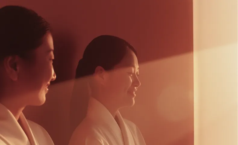 Side profile of a woman smiling softly with eyes closed, bathed in warm sunlight through a window.