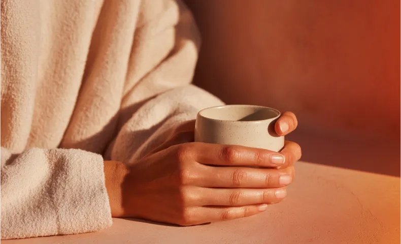 Person wearing a white robe sitting with one leg crossed, sunlight creates a warm glow on the skin and robe.