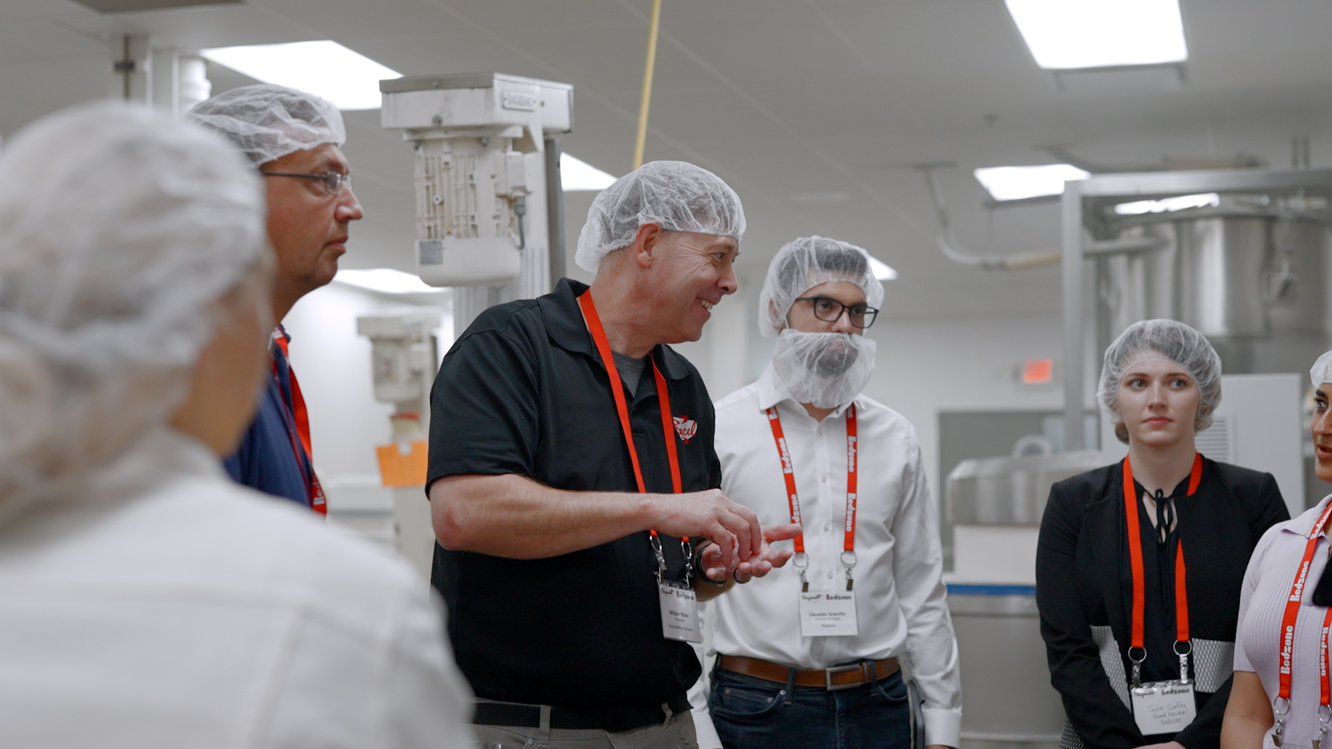 Group of people wearing hairnets and red lanyards having a discussion in an industrial or food processing facility.