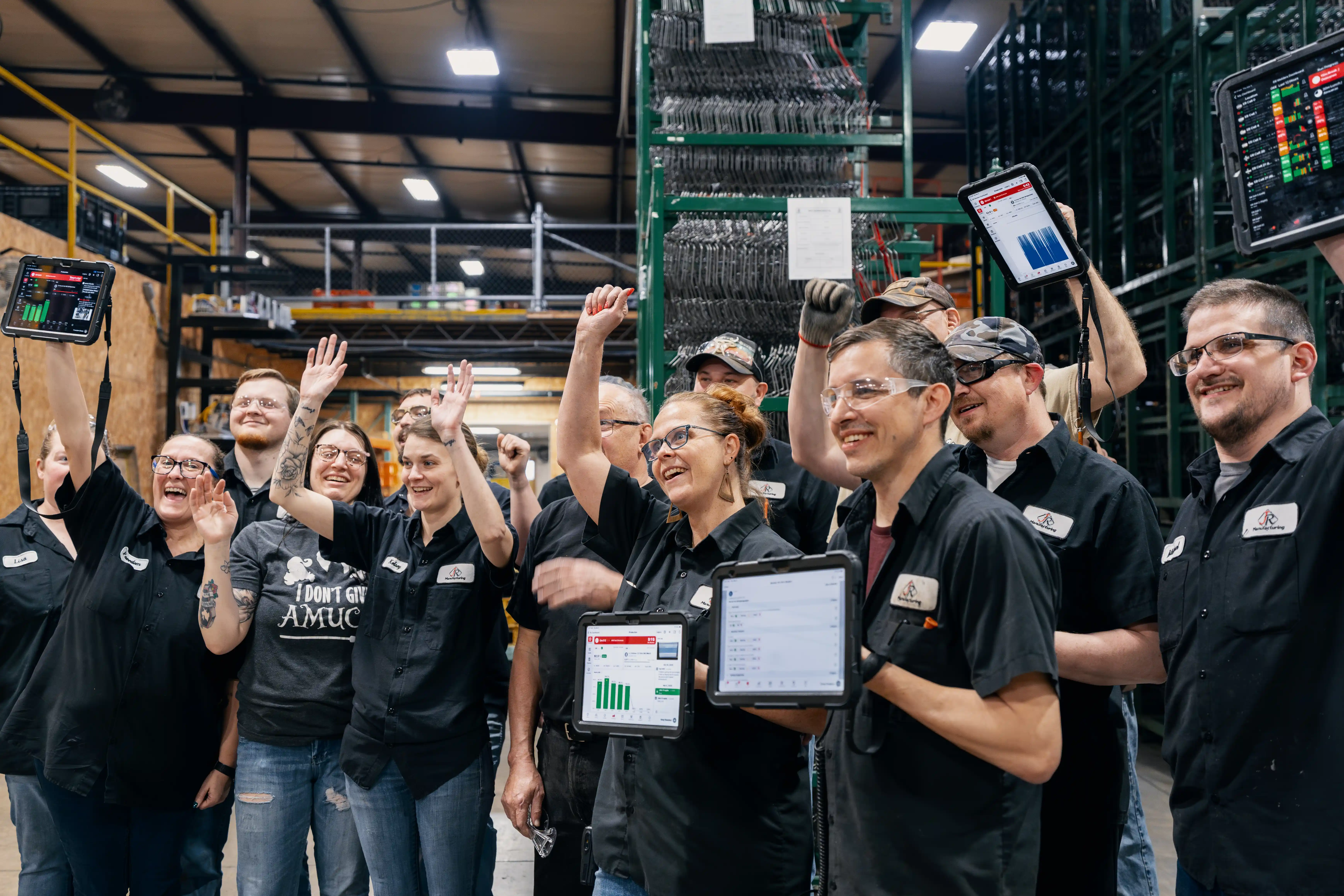 Industrial team in a warehouse celebrating with raised hands and holding tablets showing data charts.