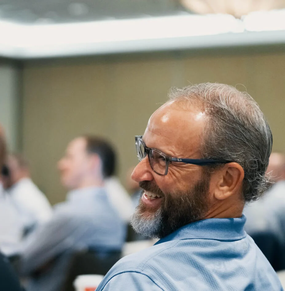 Smiling middle-aged man with glasses and a beard sitting and looking to the side in a meeting room.