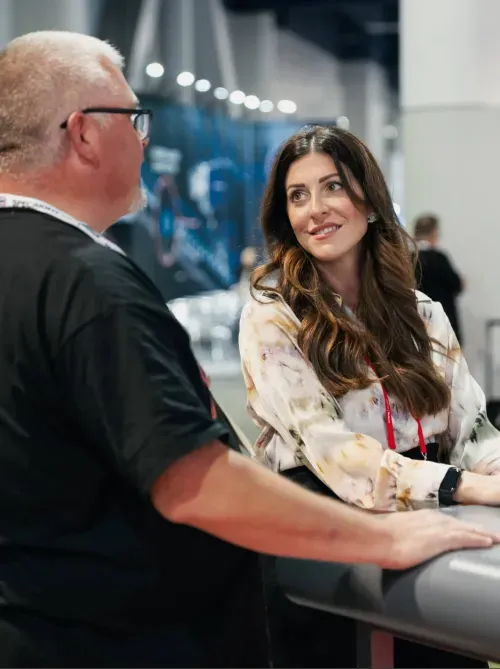 A woman with long brown hair smiling and talking to a man wearing glasses in a professional setting.