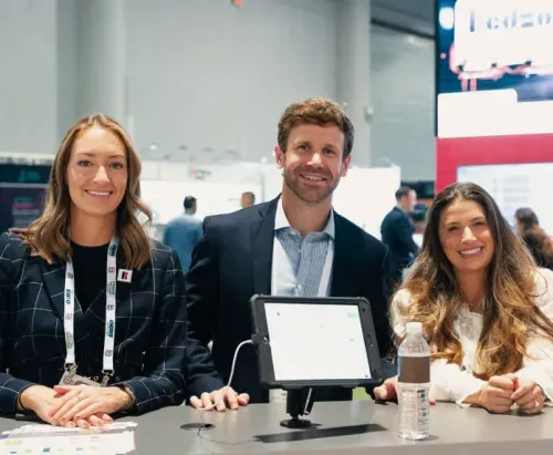 Three smiling professionals sitting at a table with a tablet and a water bottle in a conference or event setting.
