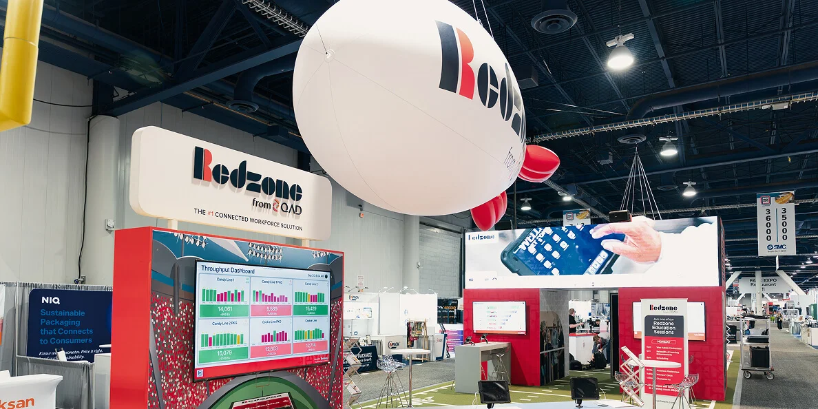 Redzone booth at a trade show with a large hanging balloon, digital screens, and interactive displays.