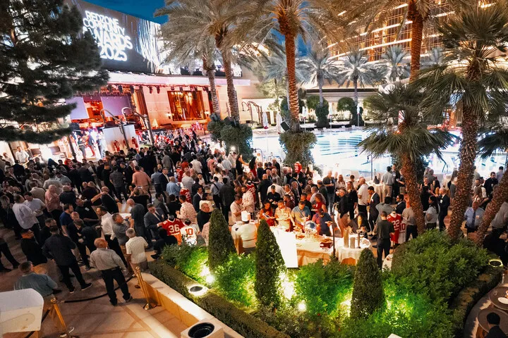 Large crowd mingling outdoors near pool and palm trees at a nighttime event with 'Redzone Community Awards' sign.
