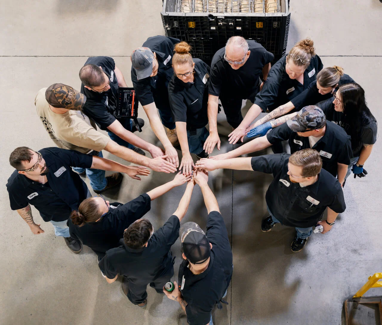 Top view of a diverse group of workers in black uniforms putting their hands together in a circle.