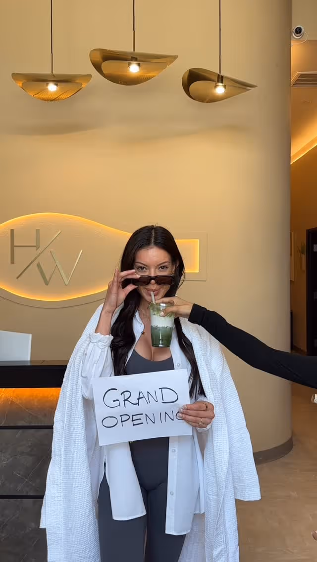 Woman wrapped in a white towel sitting with eyes closed in a warmly lit room with wooden blinds, with text "SELF CARE ISN'T SELFISH."