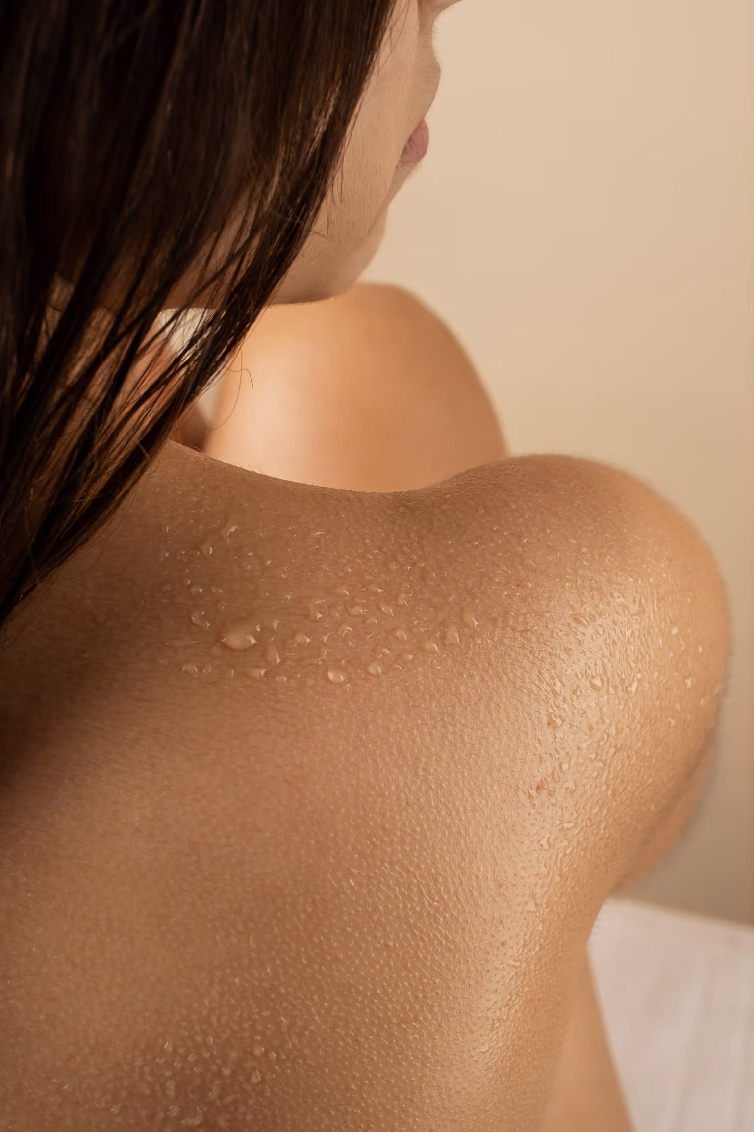 Close-up of a woman's wet shoulder and back with water droplets on skin and wet hair partially visible.