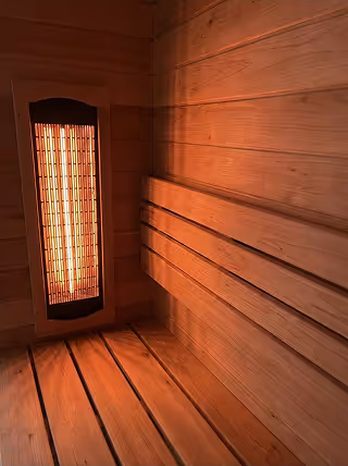 Interior of a wooden sauna with a glowing infrared heater mounted on the wall.