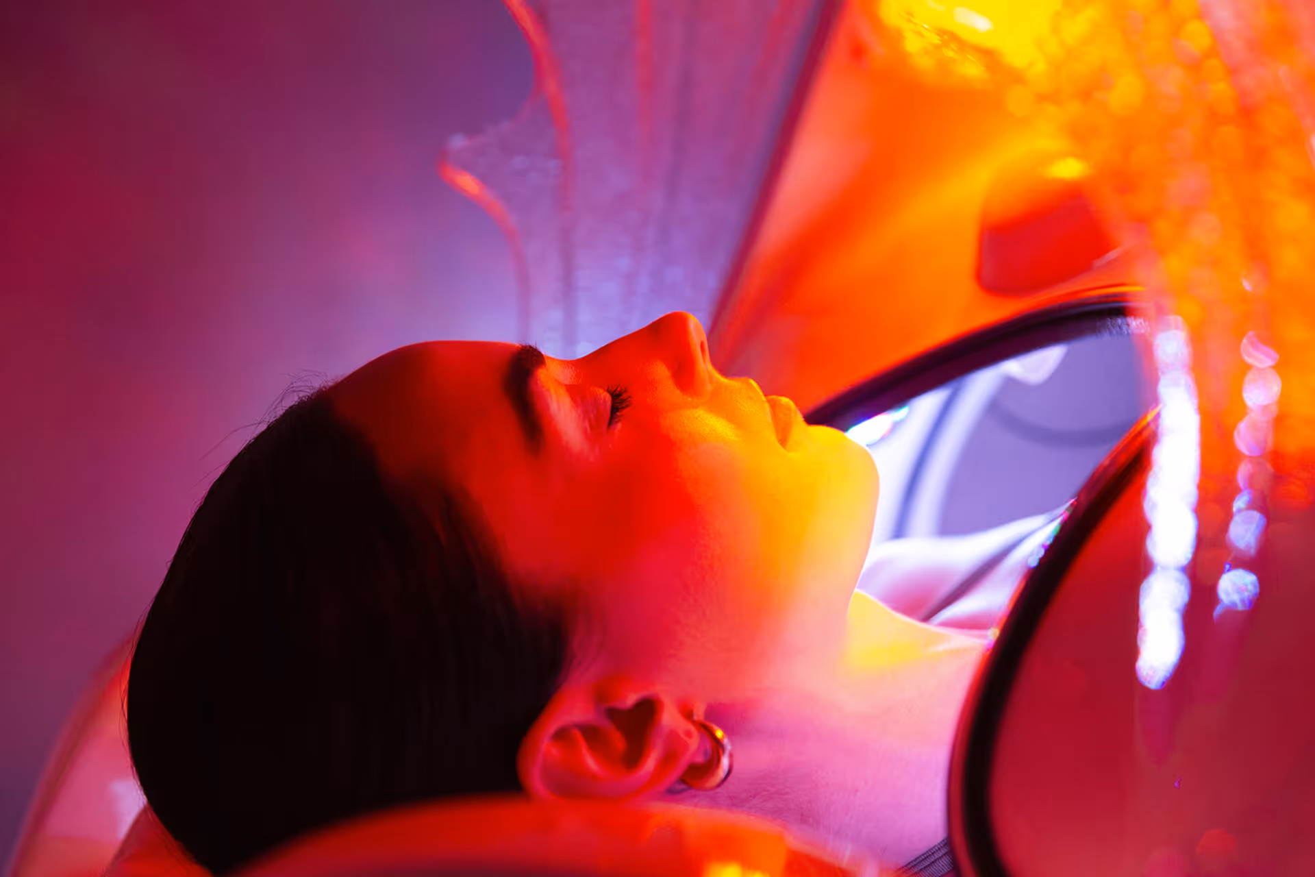Young woman wrapped in a towel sitting in a wooden sauna with steam rising from hot stones.