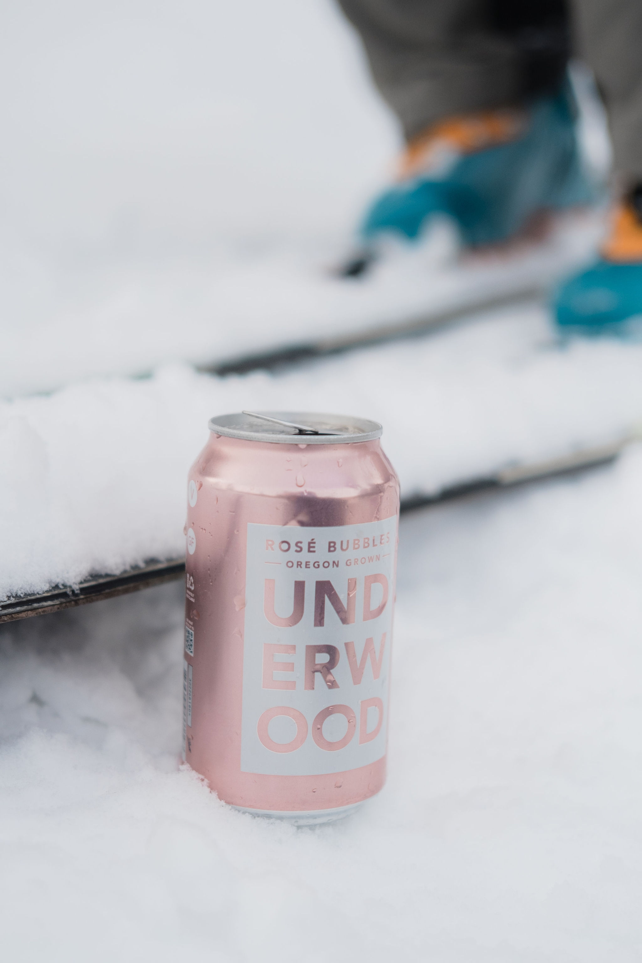 Pink can of Underwood Rosé Bubbles in snow next to skis and ski boots.