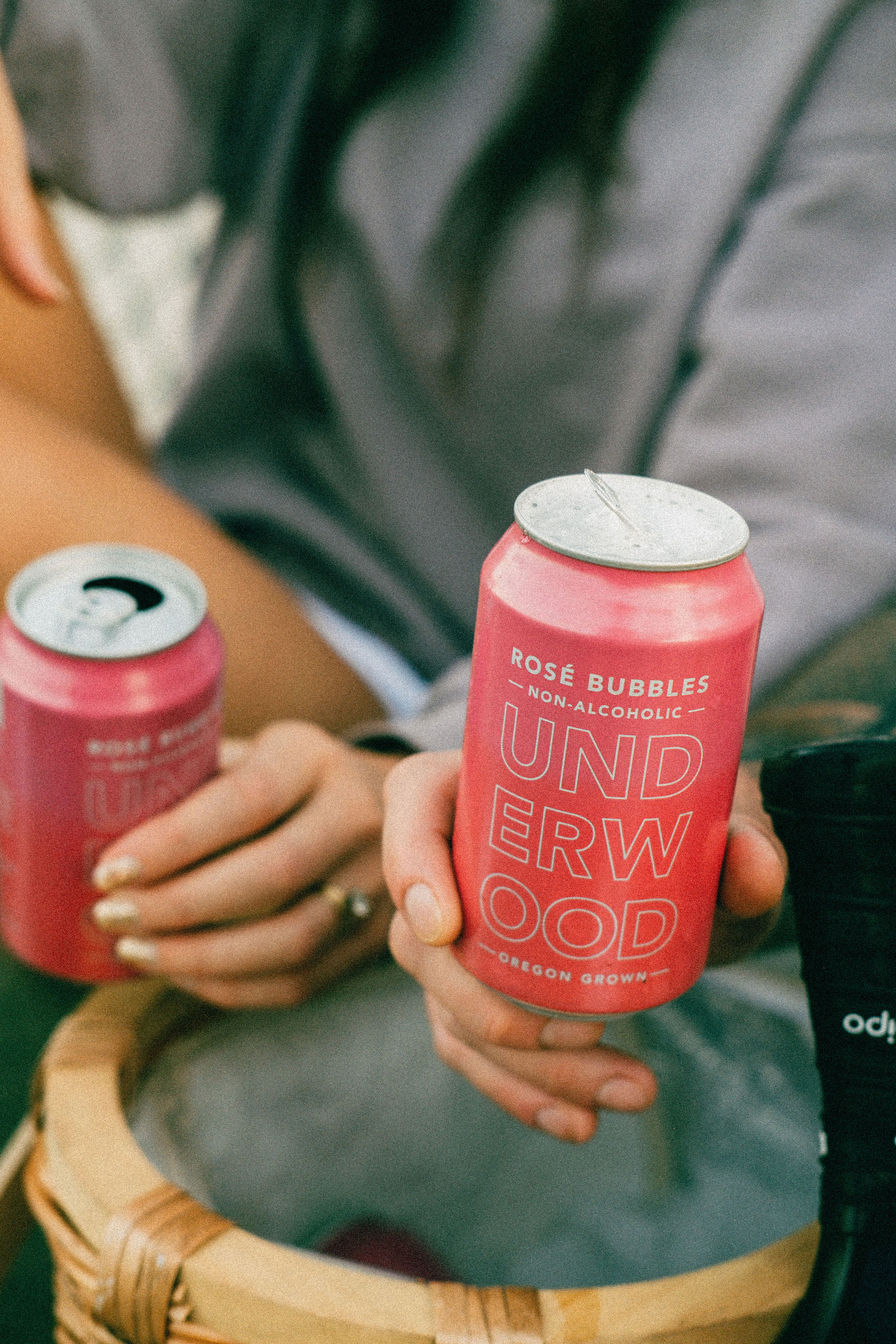 Two people holding pink cans of Underwood Rosé Bubbles non-alcoholic sparkling beverage.