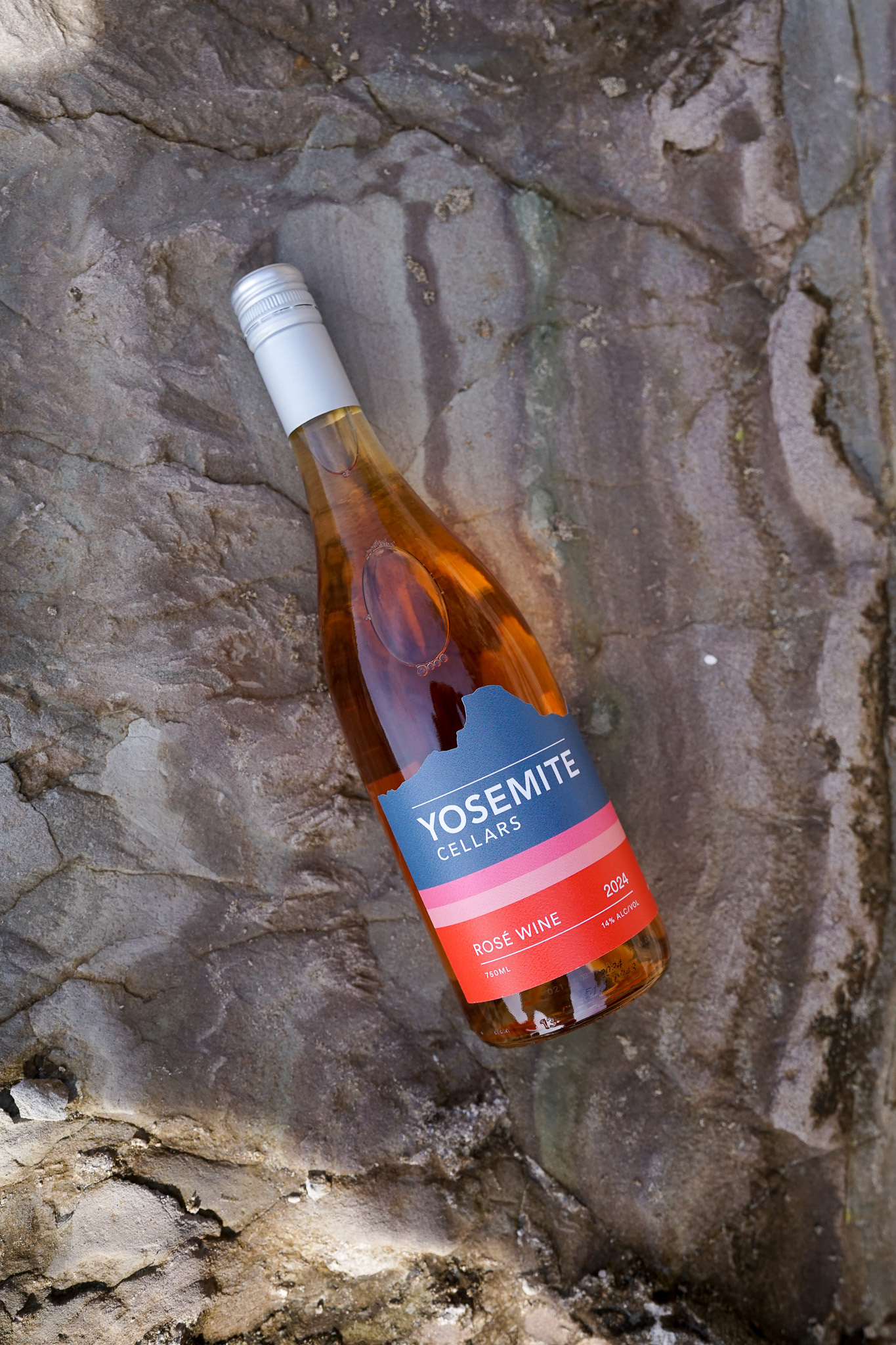 Bottle of Yosemite Cellars Rosé Wine 2024 with a silver cap lying on textured rocky surface.