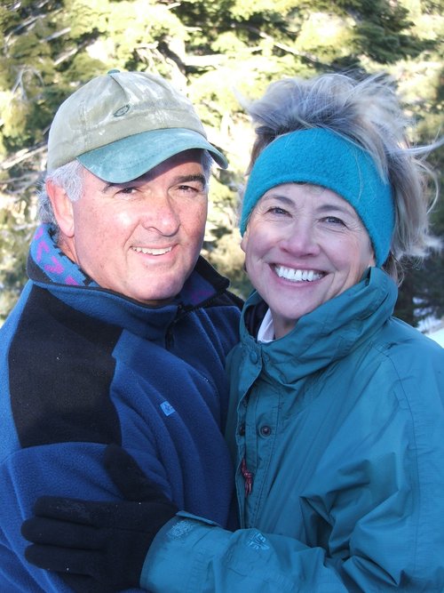 Smiling middle-aged couple dressed in winter clothing embracing outdoors with trees in the background.