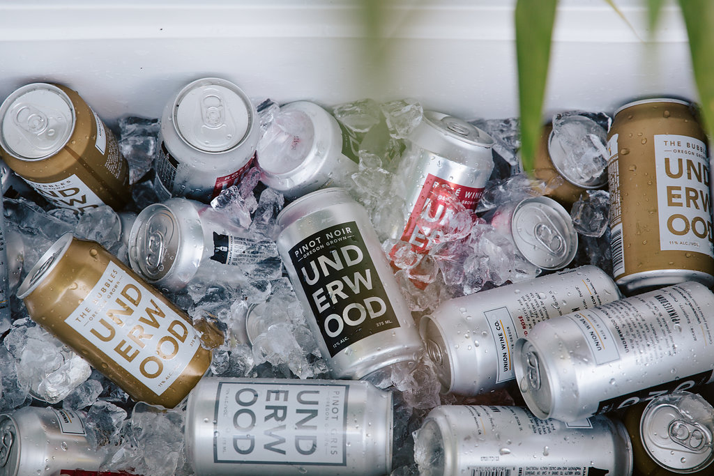Hand holding a can of Underwood Rosé Bubbles with water splashing around it.