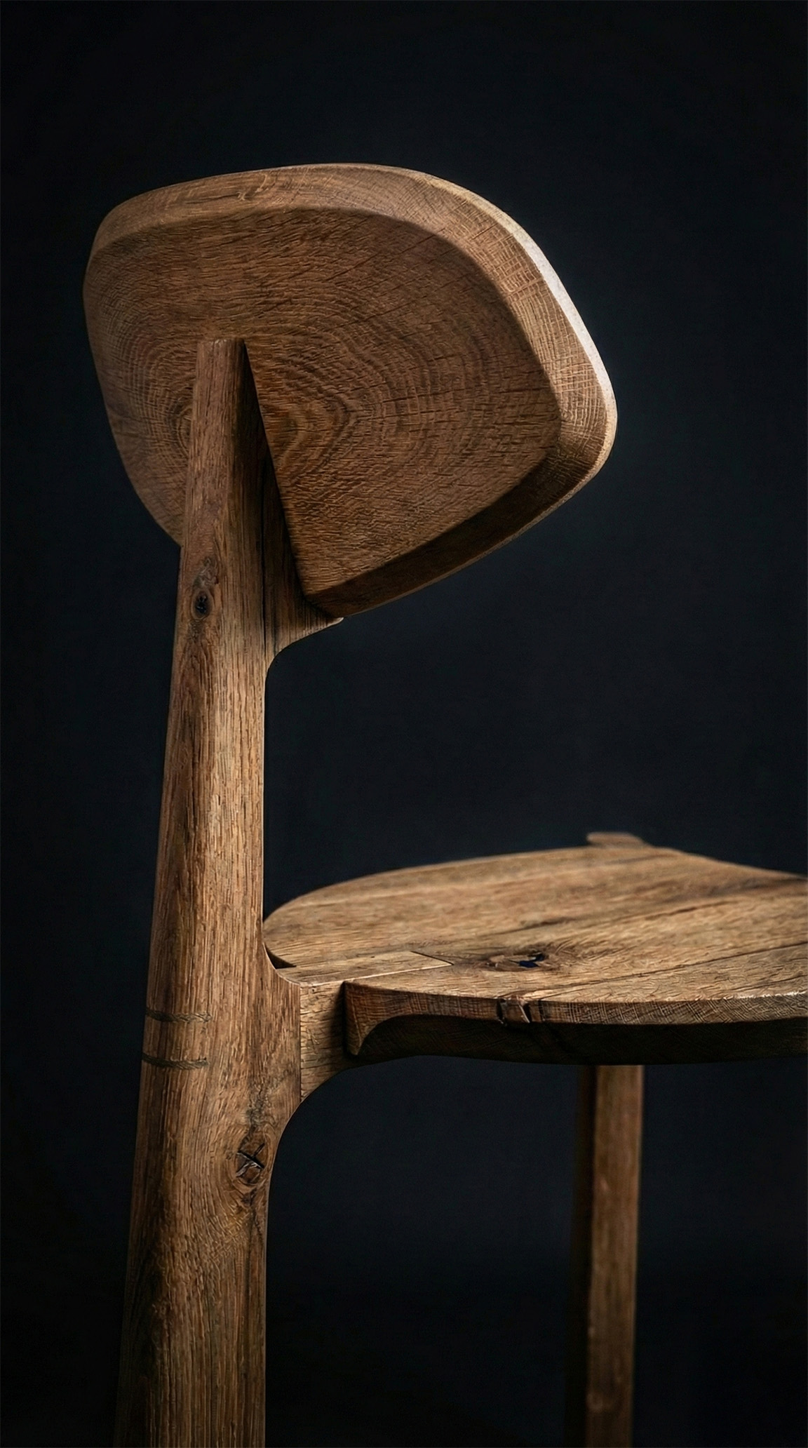 Close-up of a wooden chair backrest and seat showing detailed wood grain and craftsmanship against a dark background.