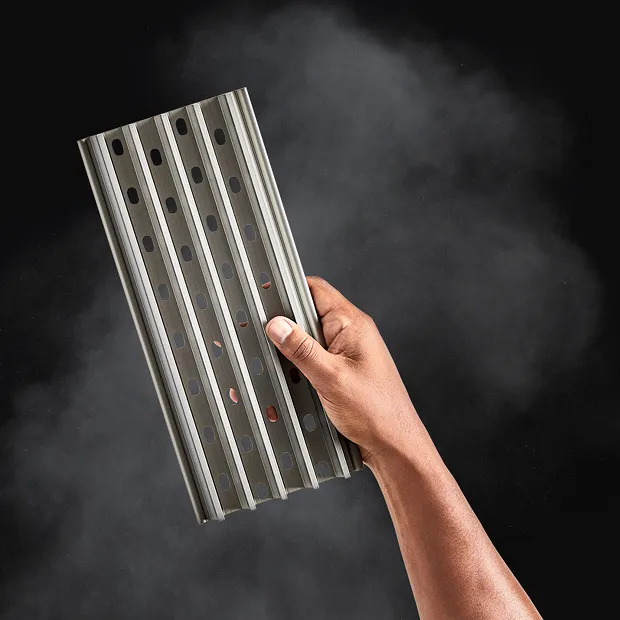 Hand holding a GrillGrate with smoke in the background