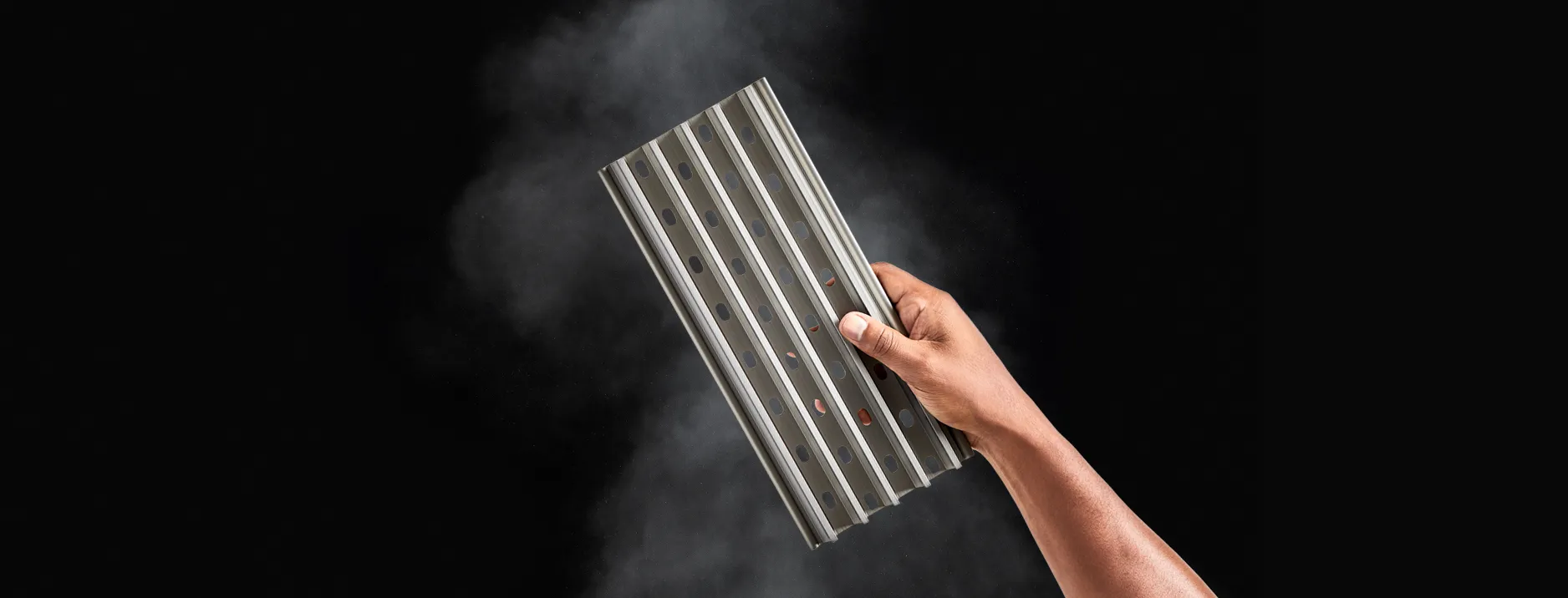 GrillGrate held by a hand with smoke in the background